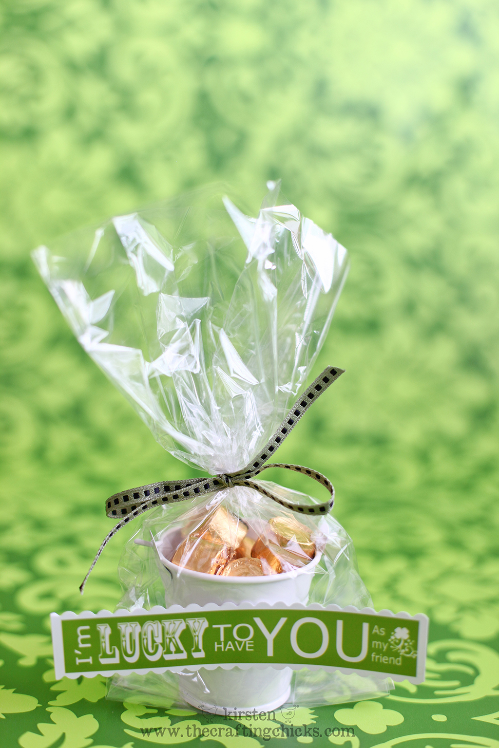 Green background withe small white buckets filled with gold wrapped candies in a clear cellophane bag and a green ribbon. A printable tag is attached that says "I'm lucky to have you."