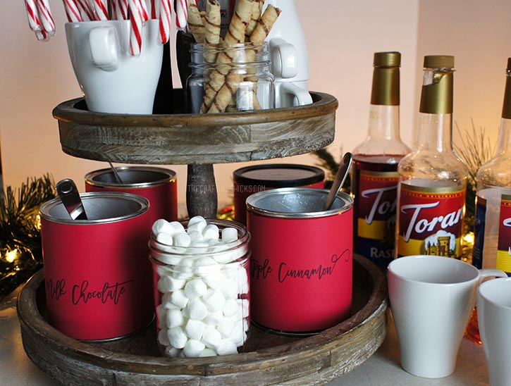 Rustic 2-tiered stand with hot chocolate mix, candy canes, marshmallow, mugs and whipped cream to make a Hot Chocolate Station.