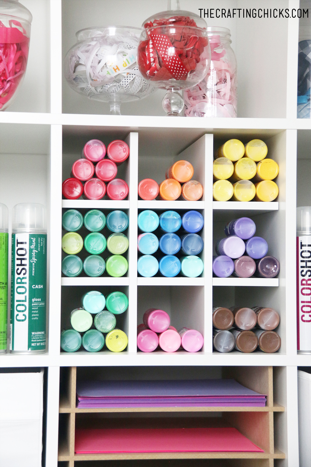 White shelves decorated with colorful jars filled with craft supplies, colorful paper, and colorful paint.