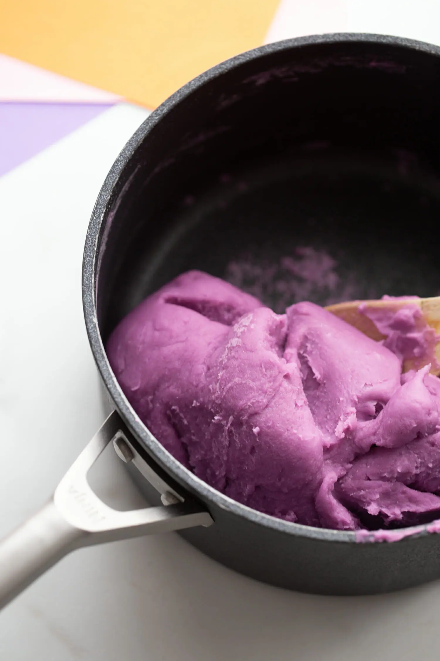 Wooden spoon mixing purple playdough together as playdough is almost fully formed.