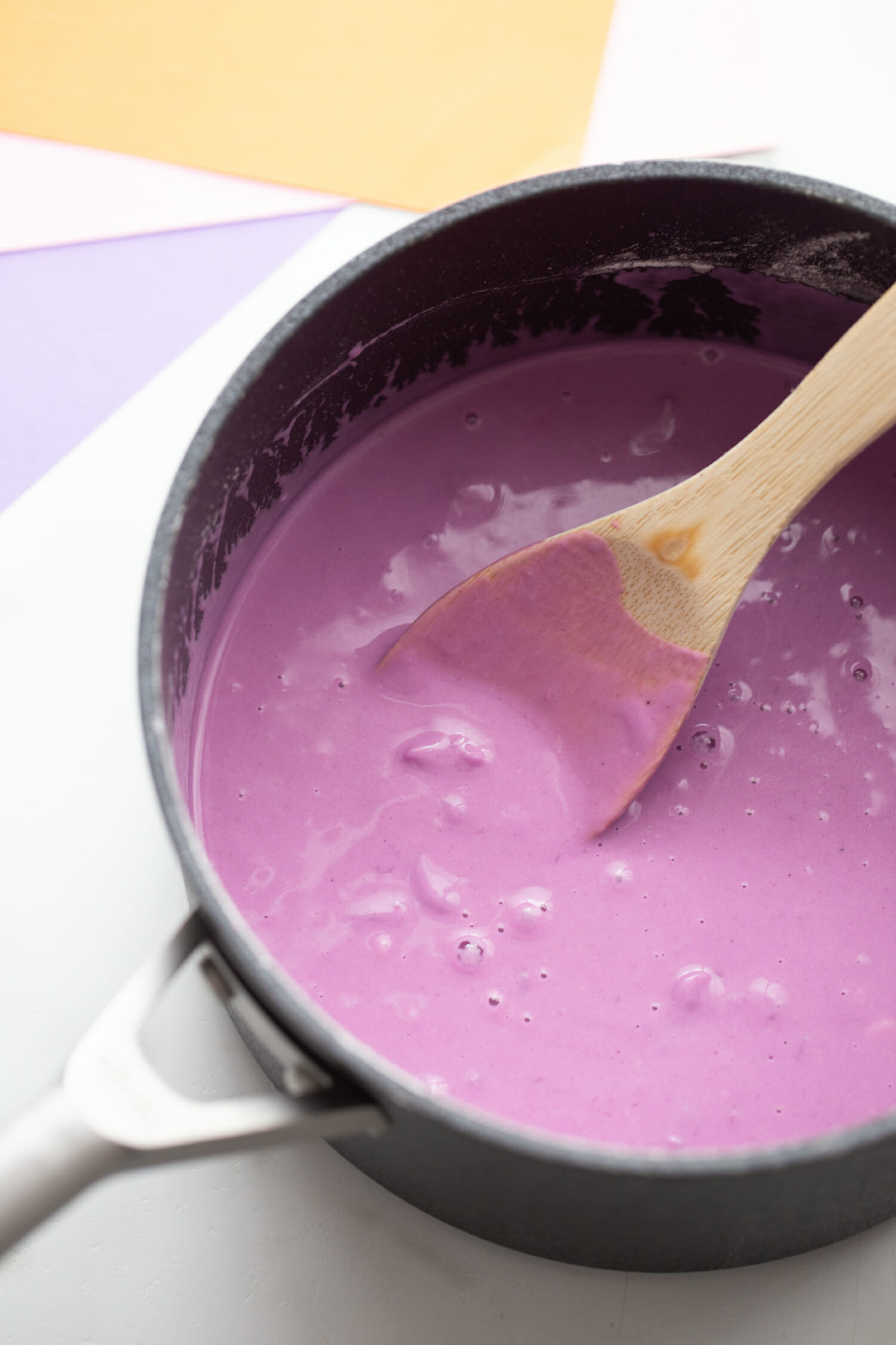Wooden spoon mixing purple playdough ingredients in a pot.