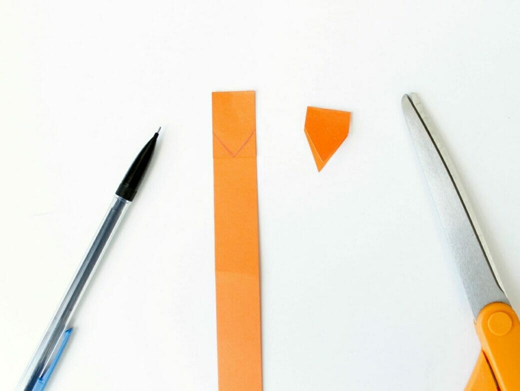 Pencil, strip of orange construction paper, and scissors on a white background.