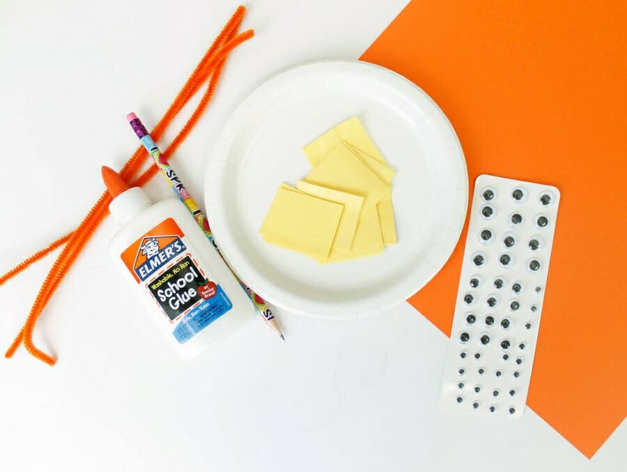 Supplies needed to make a paper plate chick craft. orange pipe cleaners, white school glue, pencil, white dessert plate, yellow tissue paper squares, orange construction paper, and googly eyes.