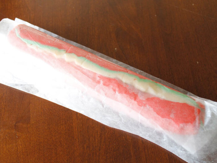 Red, Green, and white cookie dough rolled up into a log covered in plastic wrap