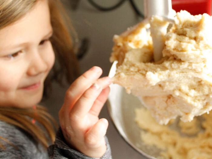 little girl taking a small piece of cookie dough from dough hook.