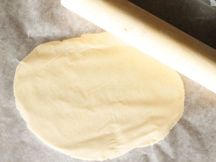 Rolling out white cookie dough layers with a rolling pin on parchment paper.