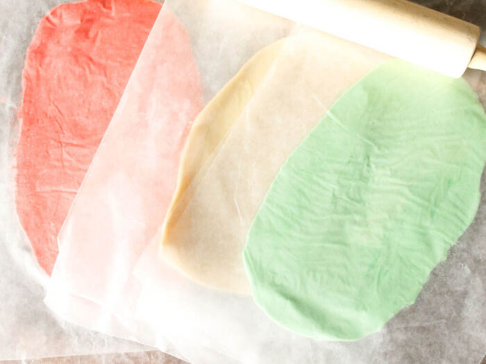 Rolled out red, green, and white cookie dough layers on parchment paper.