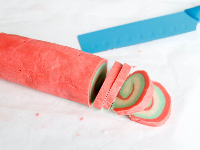 Red, green, and white cookie dough in a log cutting into slices.