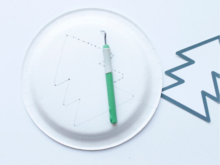 Punching holes in a paper plate for the Hand-Sewn Paper Plate Christmas Tree Craft for Kids