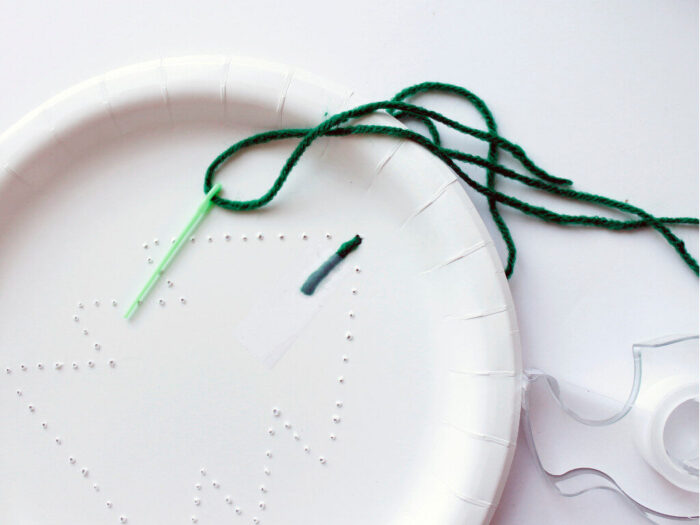 Sewing  green yarn through paper plate Christmas tree craft.