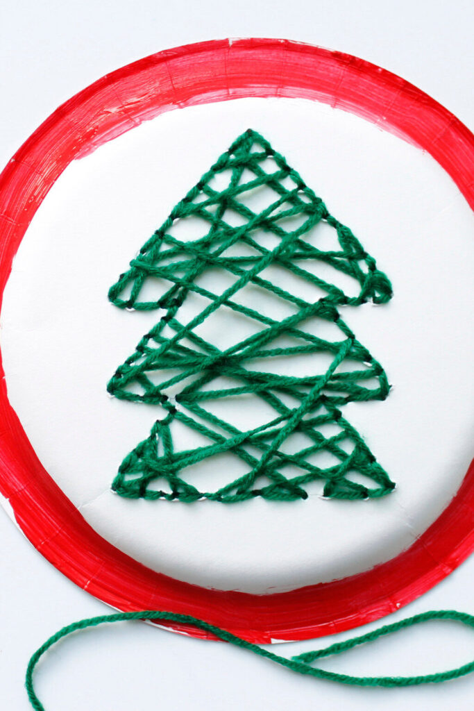 Upclose Hand-Sewn Paper Plate Christmas Tree Craft for Kids with red paint around the edges and green yarn christmas tree.