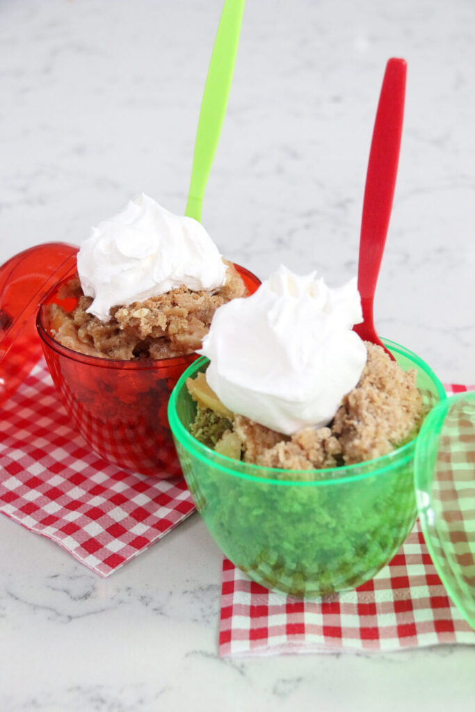 Two Baked apple crisp with golden brown oat topping with whipped topping on top.