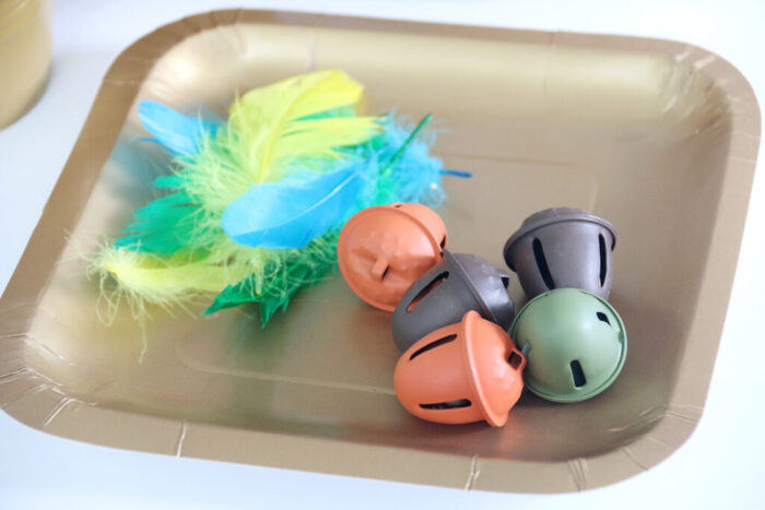 Feathers and acorn bells from the fall sensory bin on a gold paper plate.